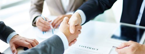 Image of business partners handshaking over business objects on workplace